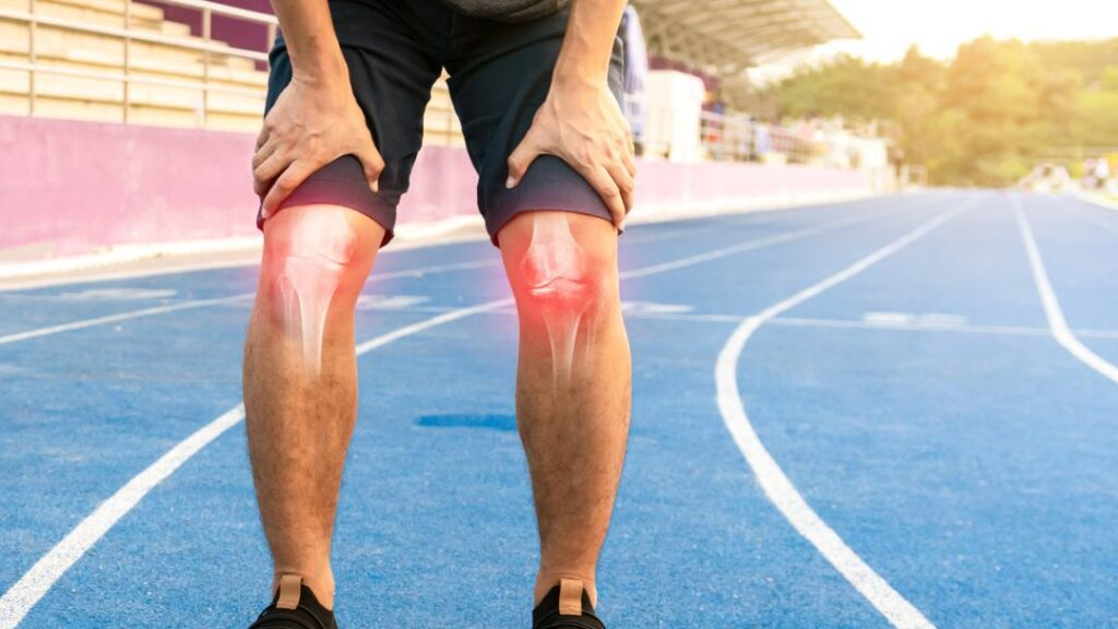 Athlete experiencing knee pain and inflammation while standing on a running track